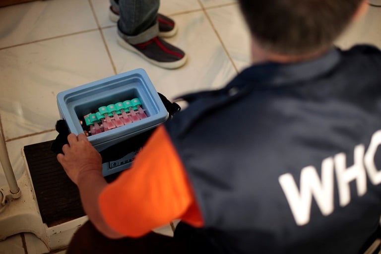 A WHO staff member looks down on an open old storage box full of vaccines.